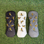 Three golf club covers with bird pattern on grass
