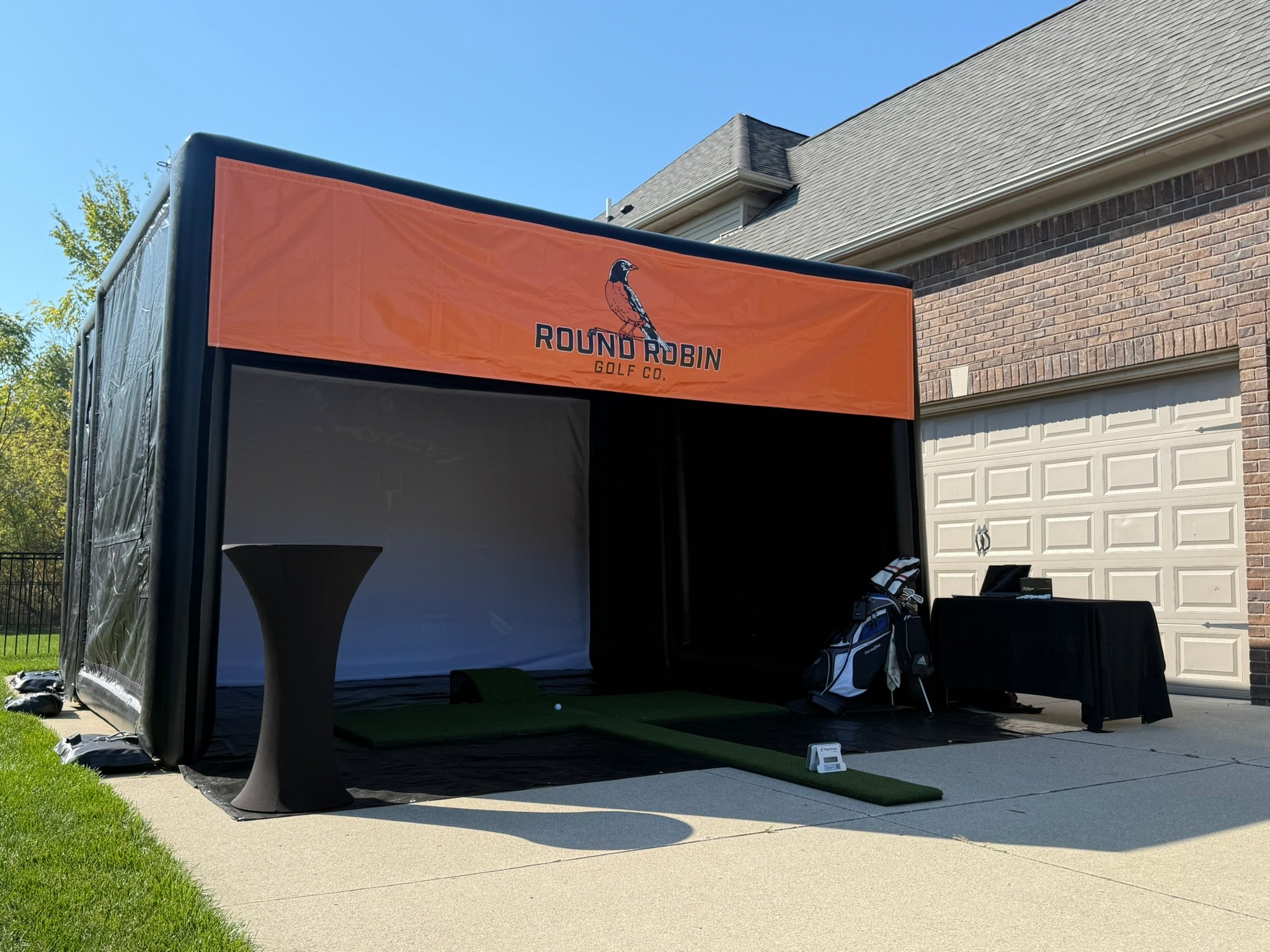 A premium portable golf simulator, placed outdoors in a driveway of a residential home. 