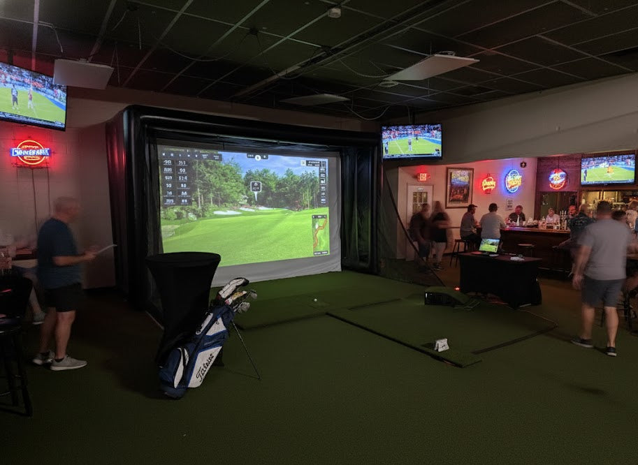 Indoor golf simulator setup with multiple screens displaying golf games in a casual setting.