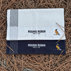 Two golf towels with 'Round Robin Golf Co.' branding on a pine needle background